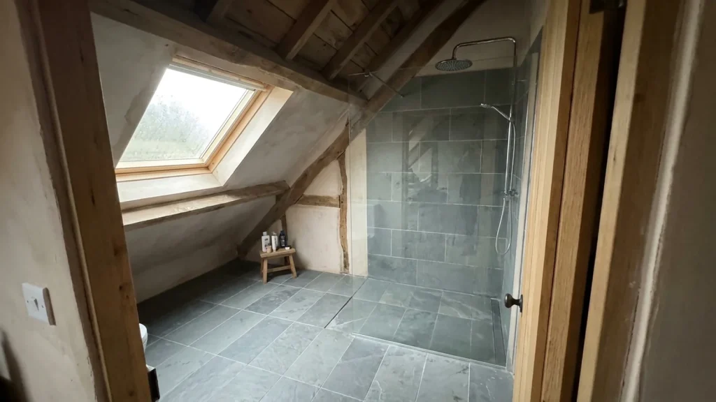 Douche à l'italienne placée dans la partie haute d'une salle de bain sous pente carrelée en gris