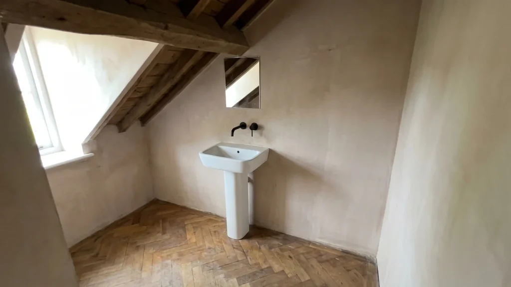 Lavabo colonne blanc en céramique installé dans un angle de salle de bain mansardée avec parquet chevron